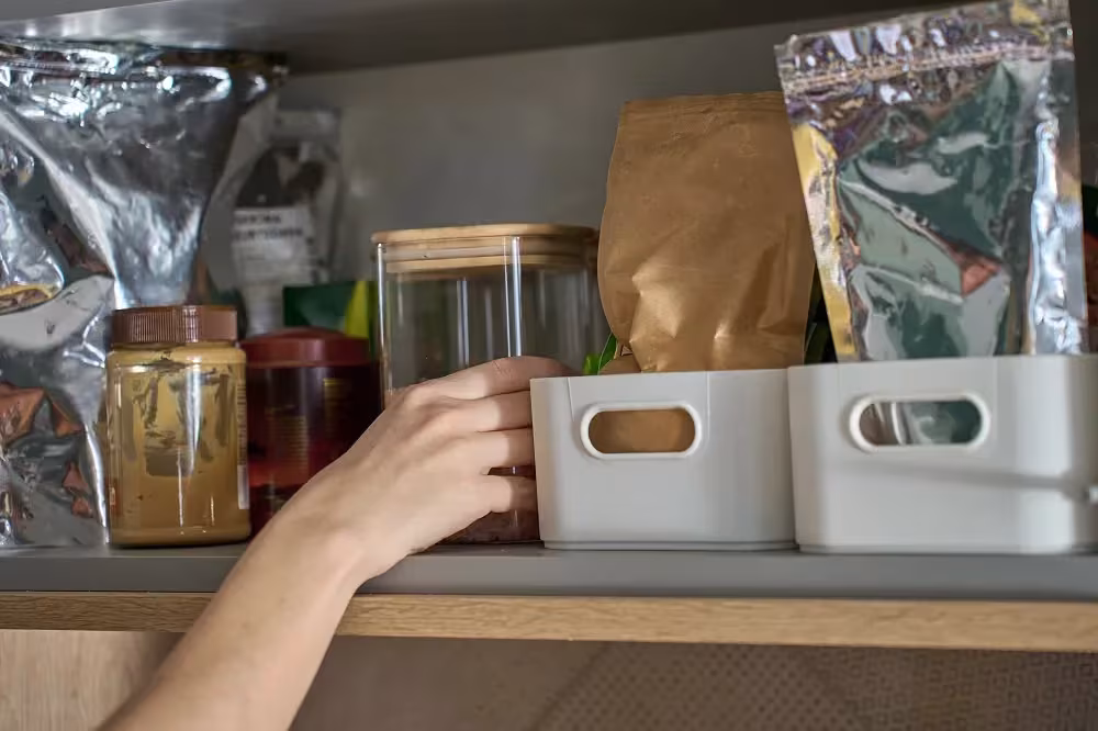Hand reaching for a storage bin on an open pantry shelf