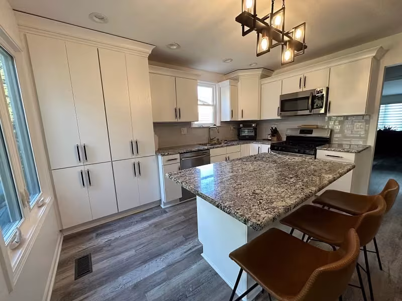 White refaced cabinets and a granite island with seating in the Bartlett kitchen