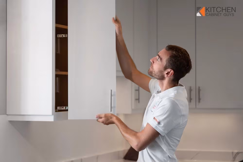 Technician fitting a white panel to a cabinet in a bright kitchen