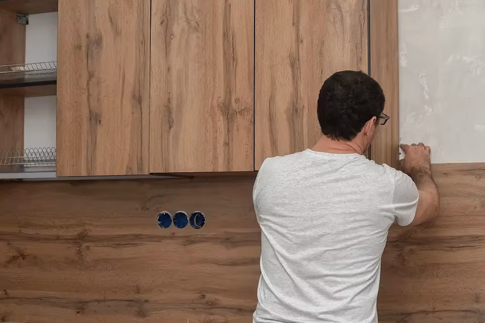 Man applying a woodgrain panel to a wall cabinet