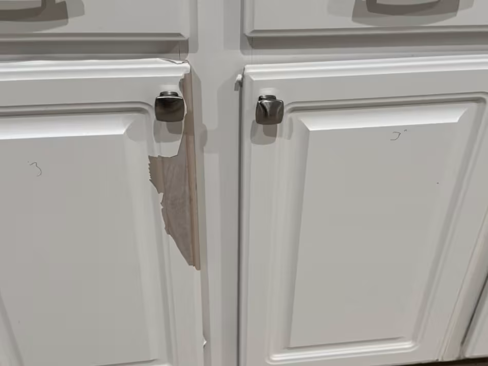 Peeling thermofoil across the face of two white cabinet doors