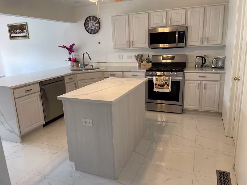 Cream cabinets and a gray painted island over tile flooring in a Chicagoland kitchen