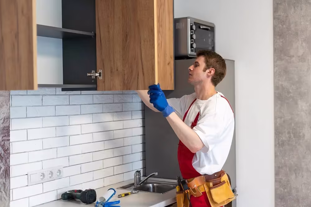 Worker in an apron fitting a wood cabinet above a subway tile backsplash