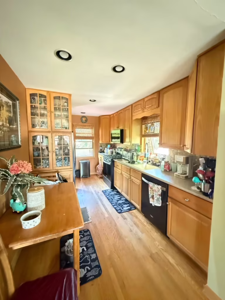Honey oak galley kitchen with orange walls and black appliances before refacing