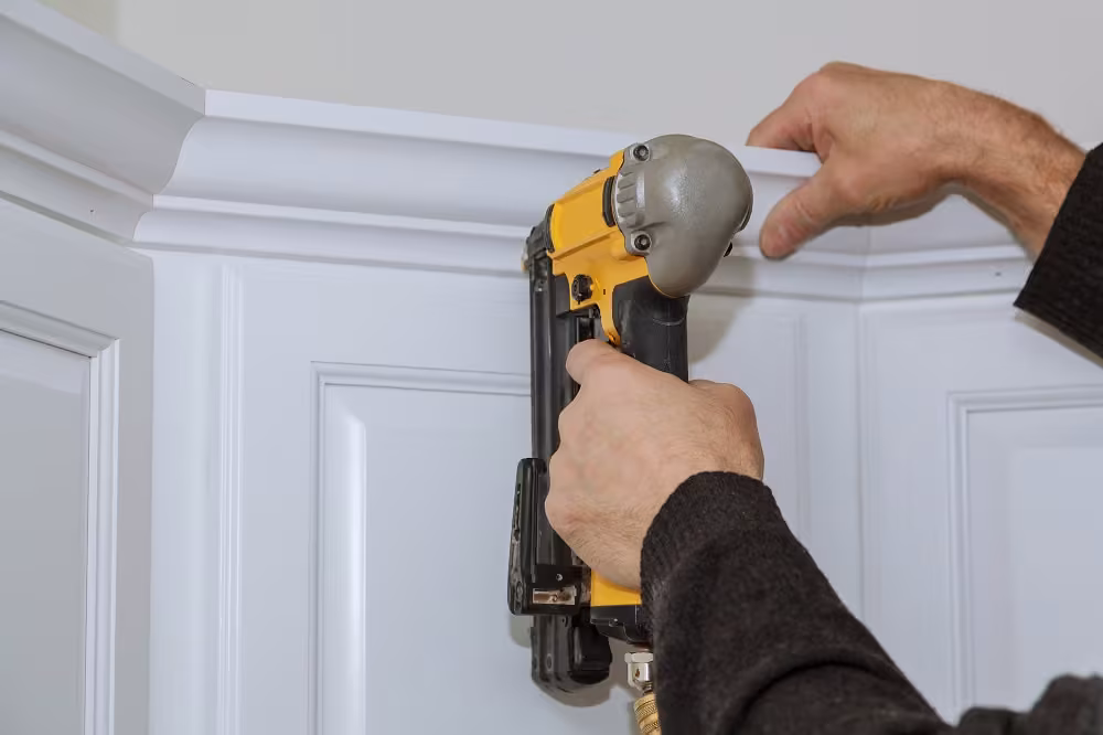 Hands nailing crown molding onto refaced white wall cabinets