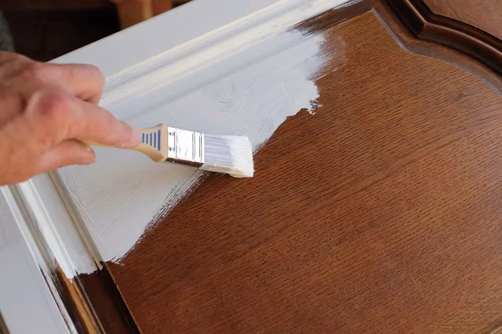 Brush painting white over a dark wood cabinet door