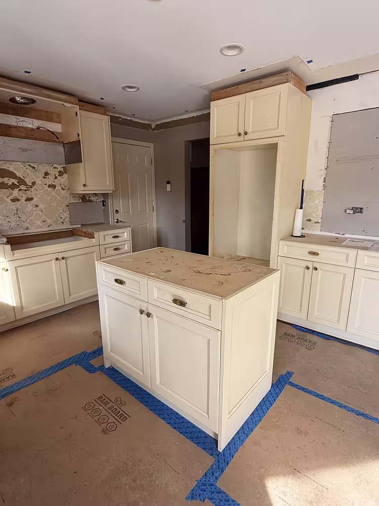 Cream raised panel cabinets and island masked off at the start of refacing