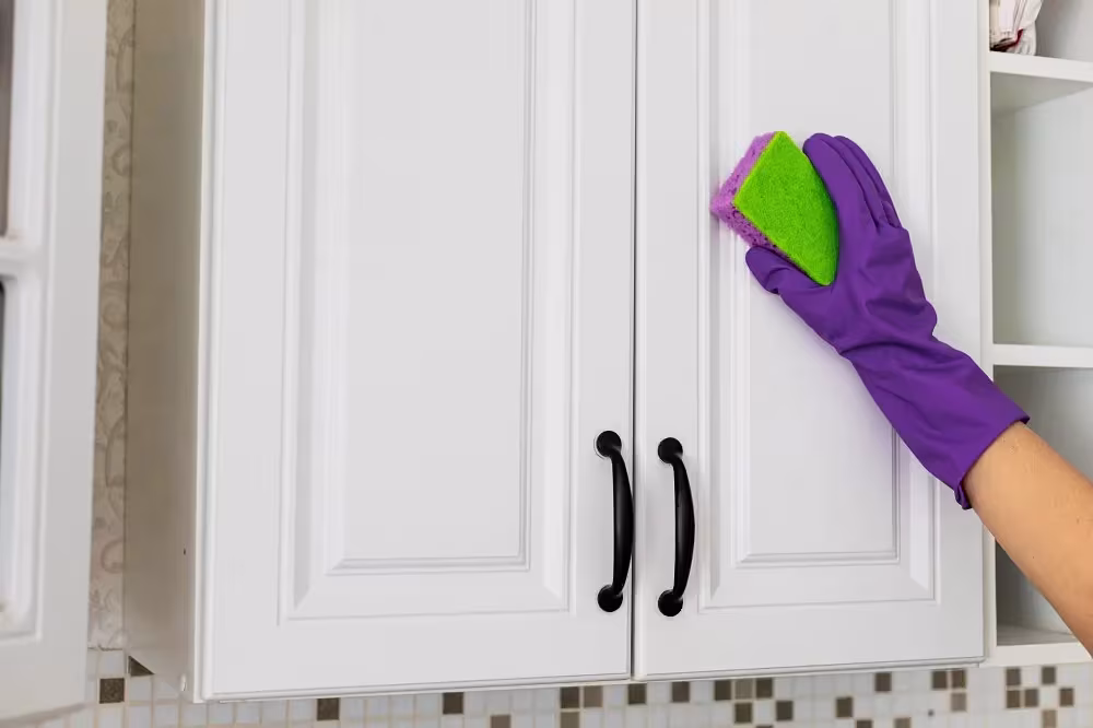 Gloved hand wiping a white cabinet door with a sponge