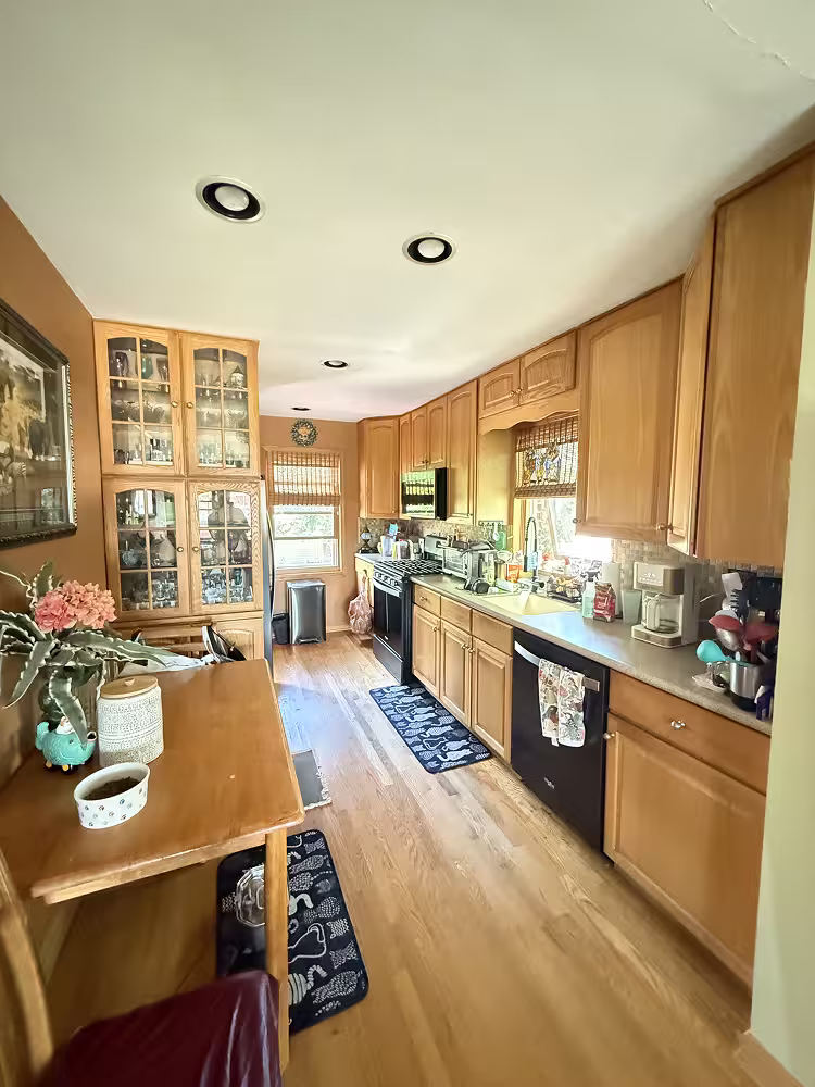 Honey oak galley kitchen with orange walls and black appliances before refacing