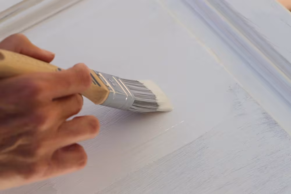 Hand brushing fresh paint across a cabinet surface