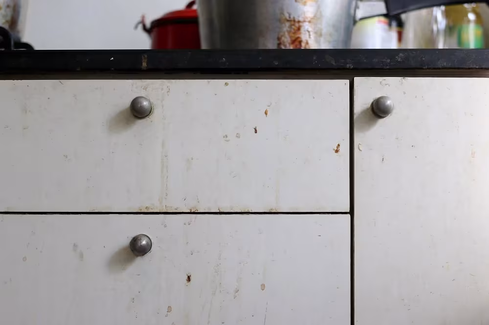 Worn cream drawer fronts with dark knobs on an ageing kitchen