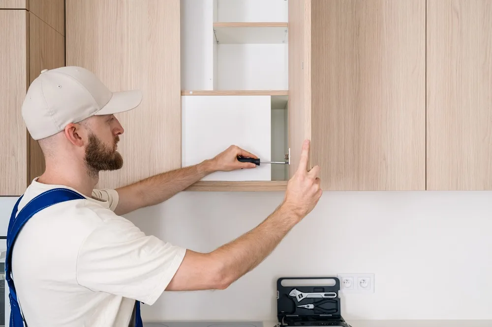 Technician fitting a light wood cabinet panel during a thermofoil repair