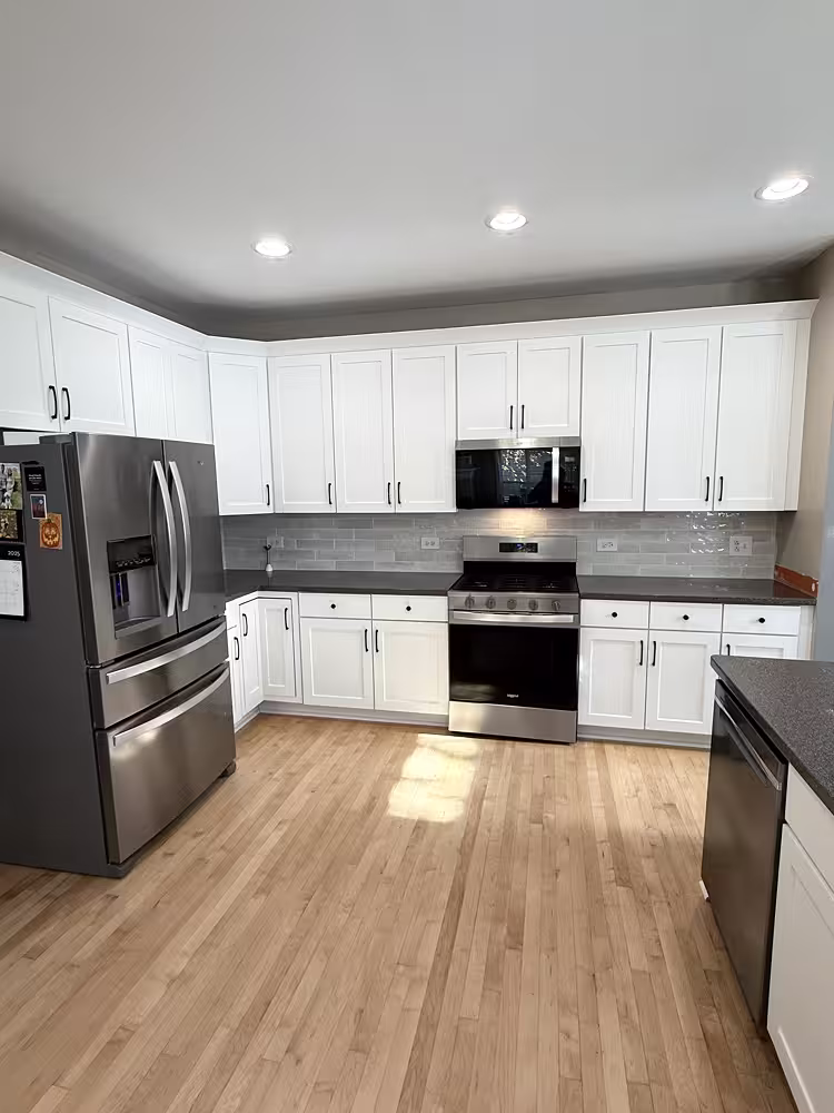 White Shaker cabinets above gray counters after refacing the oak kitchen