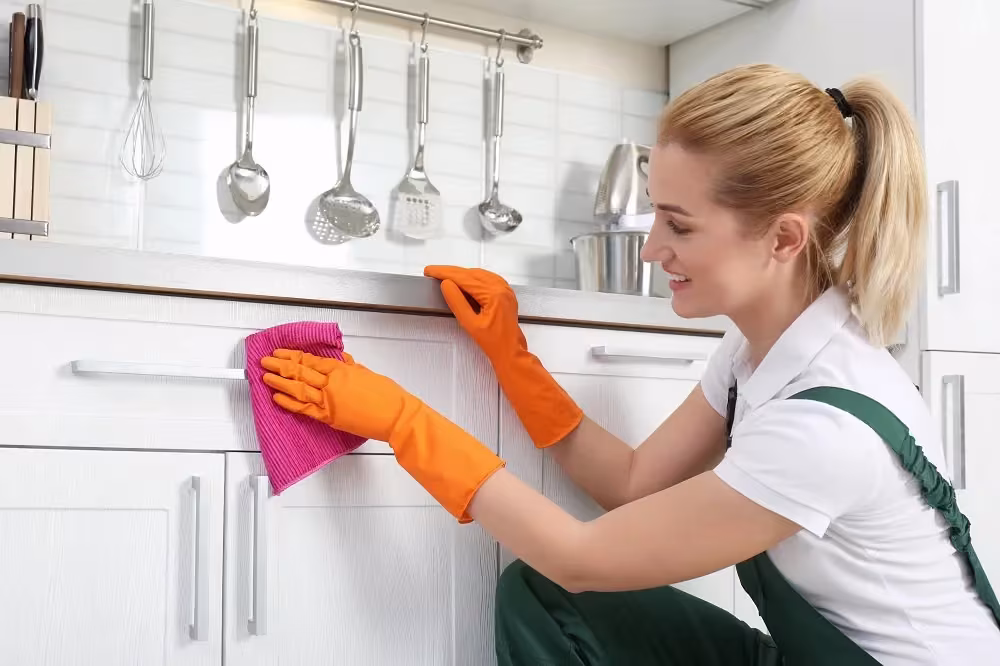 Woman in rubber gloves wiping a white cabinet door clean