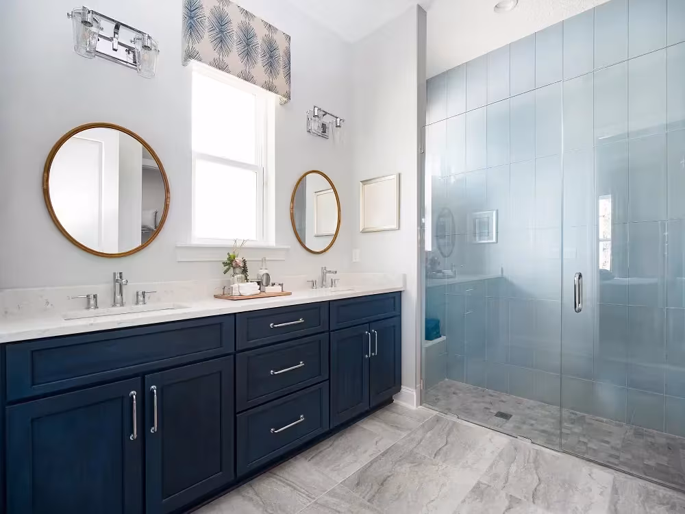 Navy blue bathroom vanity with twin round mirrors and a walk-in shower